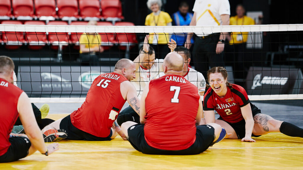 Members of the Canadian volleyball team laughing and stretching on the gym floor