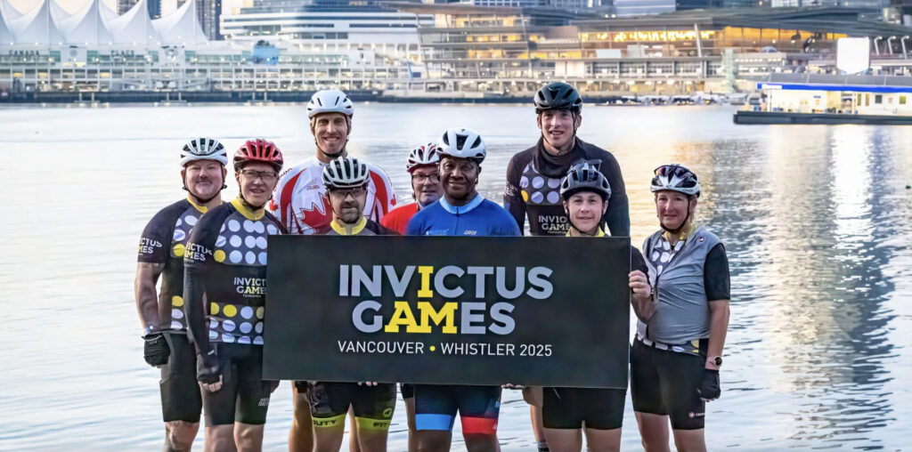 Cyclists standing together holding an Invictus Games Vancouver Whistler poster
