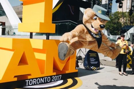 A mascot of a bear jumping by a sign saying "I am Invictus"
